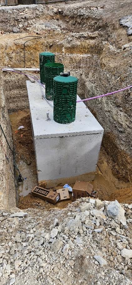 Three green septic tanks mounted on a concrete foundation in an excavation during a new install